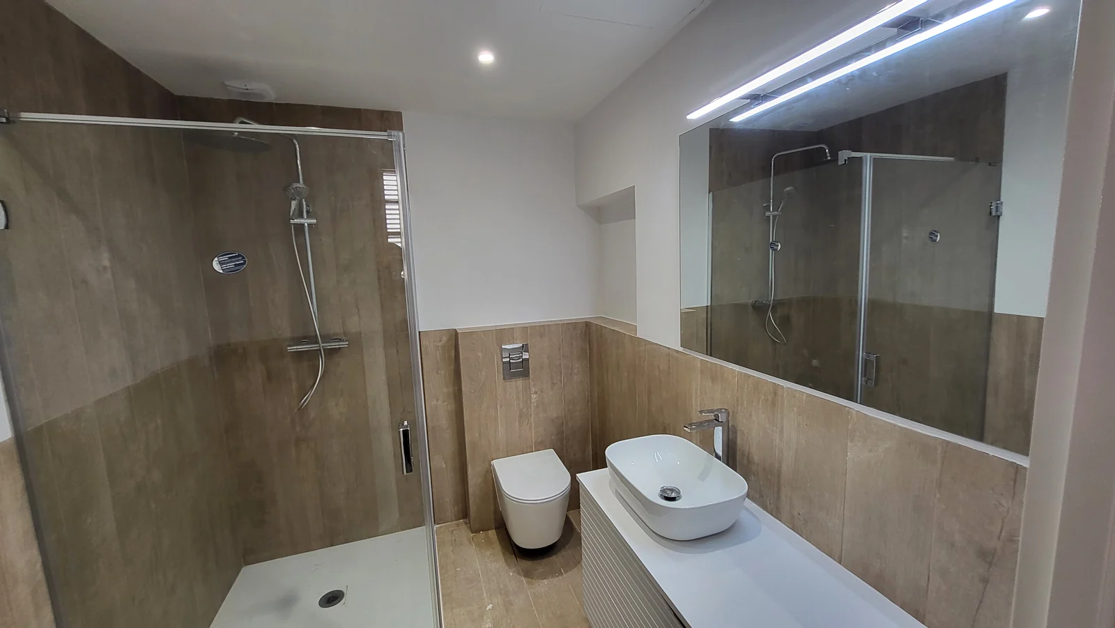 Bany acabat amb dutxa, lavabo i mirall il·luminat